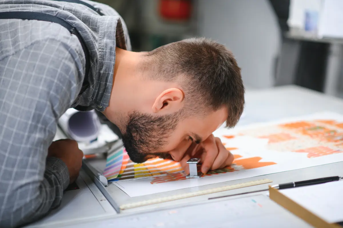 Print technician closely inspecting DTF print quality and color registration with a magnifying loupe
