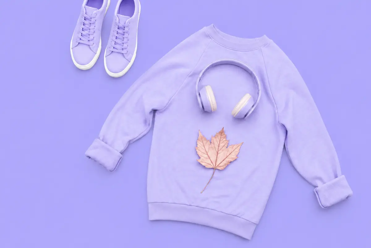Flat lay of a lavender sweatshirt with headphones and a maple leaf, paired with matching sneakers on a purple background