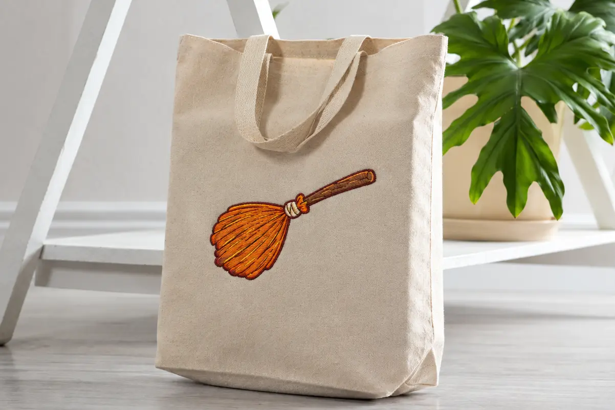 Custom embroidered Halloween tote bag featuring an orange witch broom design